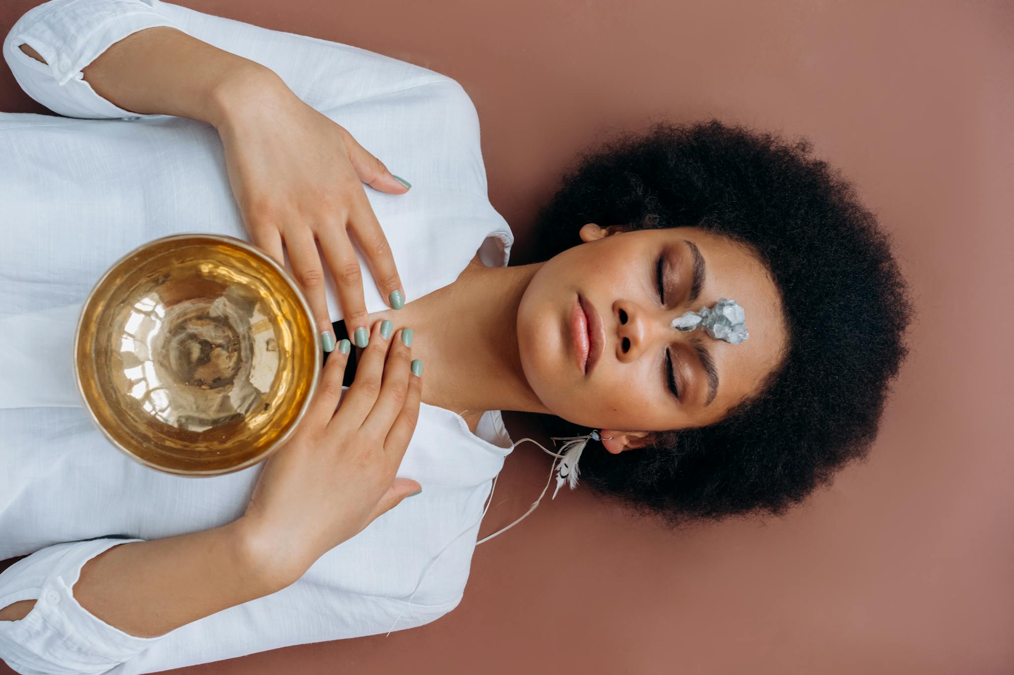 A woman meditates with a Tibetan singing bowl and crystals, promoting wellness and spiritual healing.