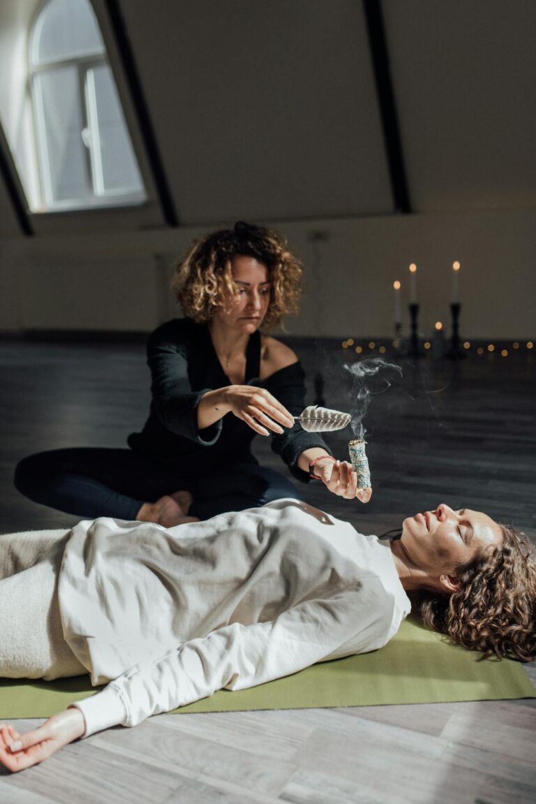 A woman performs a healing ritual with sage smoke indoors, aiding in meditation and tranquility.