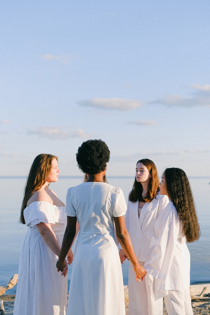 A group of multicultural women holding hands by the sea, enjoying a tranquil summer evening.