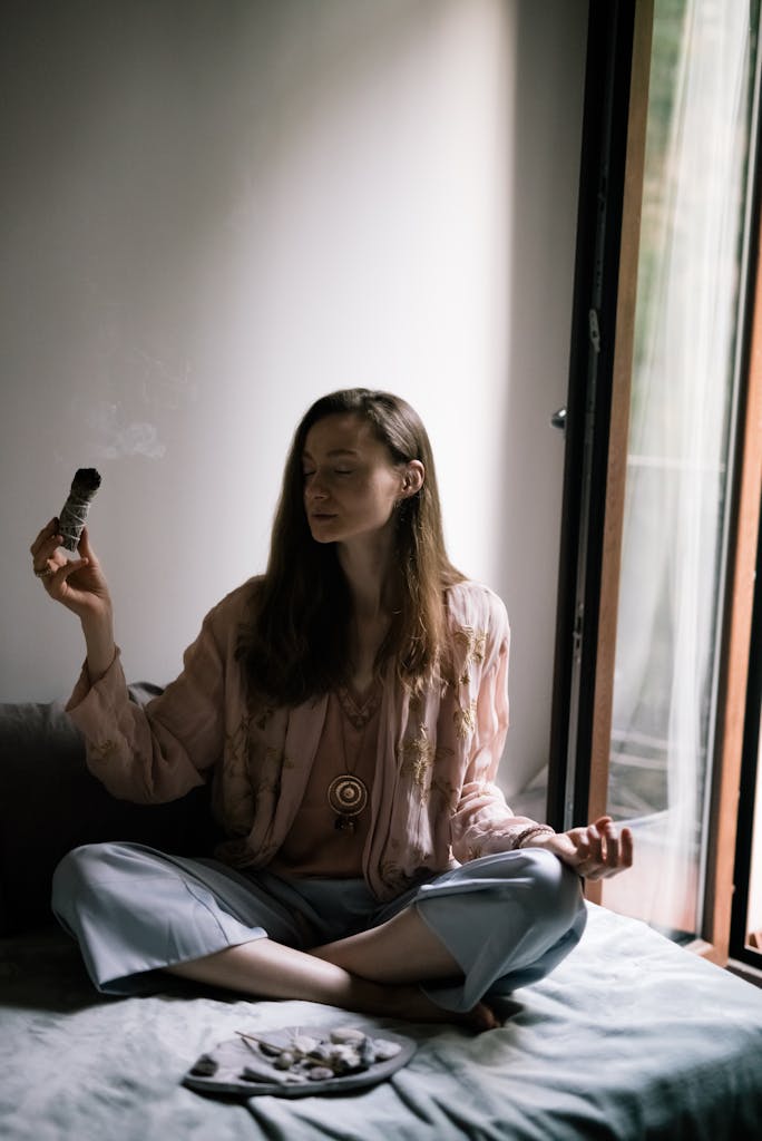 Calm and serene indoor meditation scene with a woman holding sage and smoke.